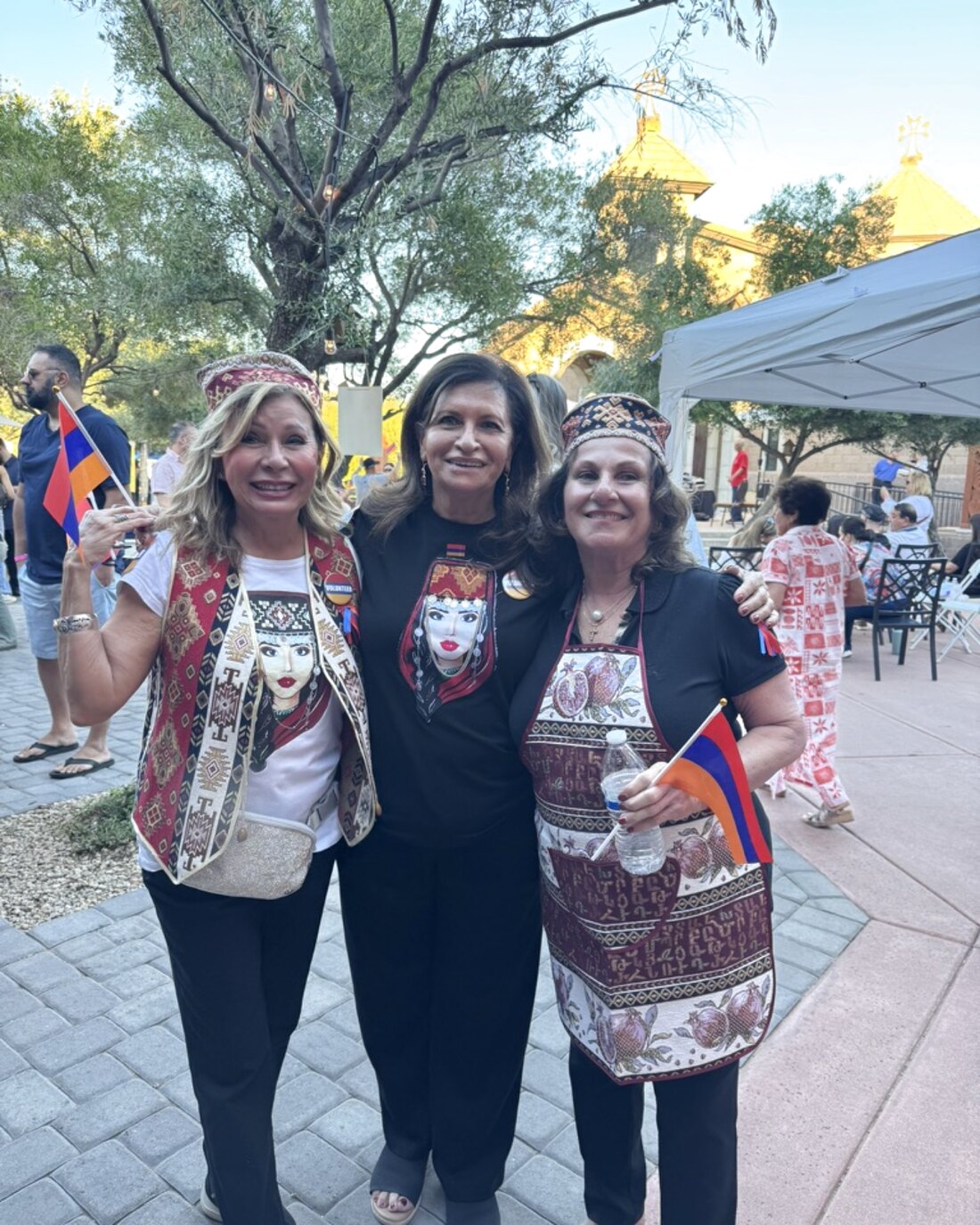 Three women in embroidered Armenian vests holding Armenian flags