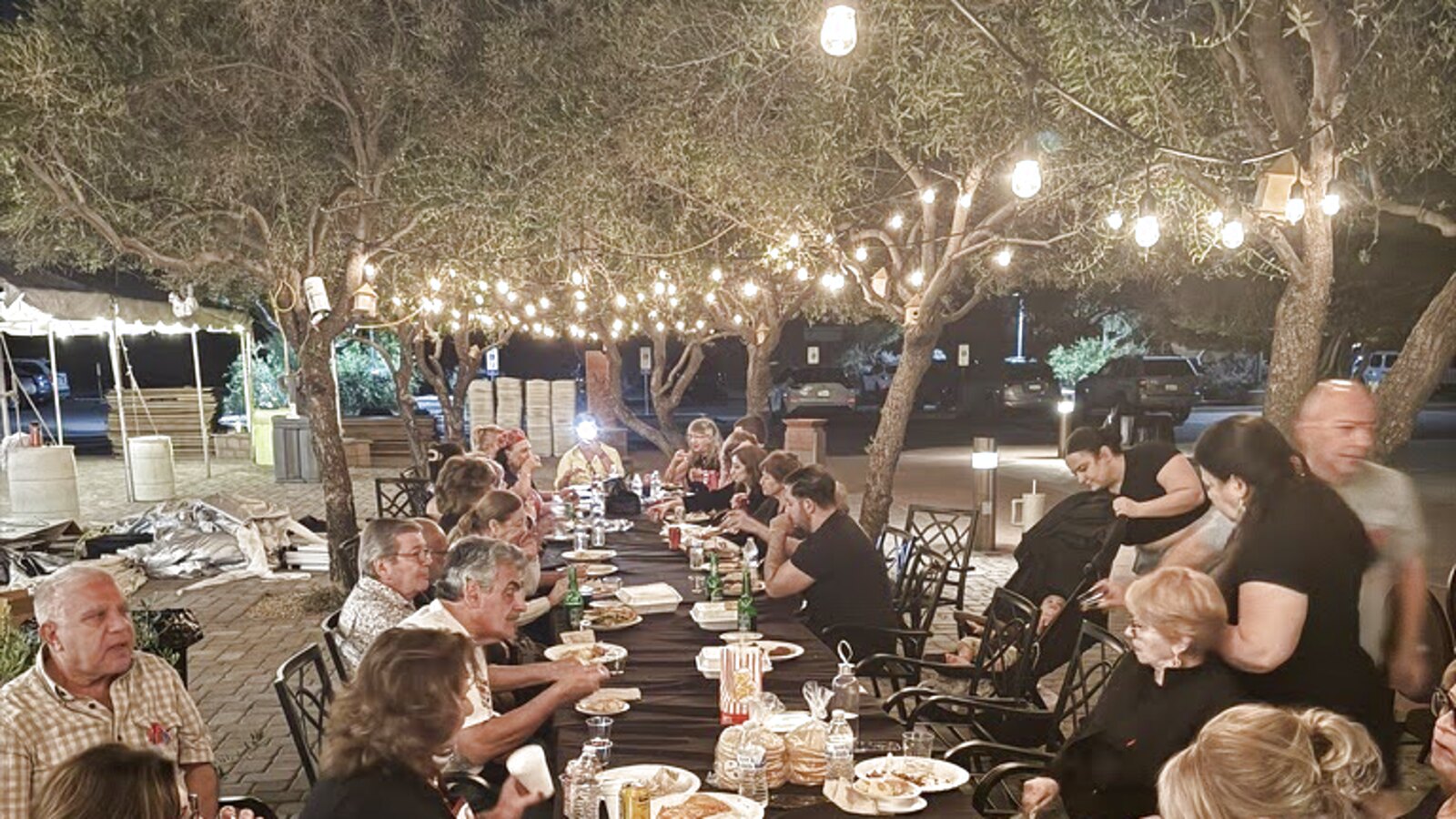 Guests eating at long tables under string lights in the courtyard